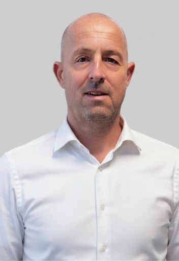 Portrait von Holger Günsch, Inhaber von Zenker & Günsch Immobilien, lächelnd im weißen Hemd vor neutralem Hintergrund.